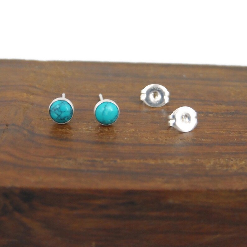 May include: A pair of silver stud earrings with turquoise stones. The earrings are on a wooden surface.