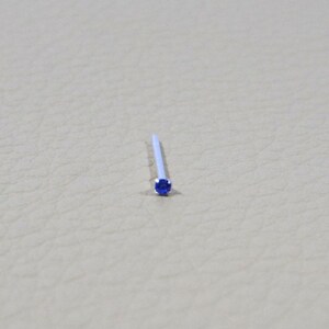 Op de afbeelding: Een kleine, zilveren neusring met een blauwe edelsteen.