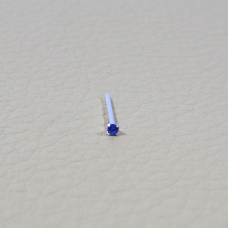 Op de afbeelding: Een kleine, zilveren neusring met een blauwe edelsteen.