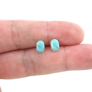 May include: A pair of oval turquoise stud earrings with silver settings.