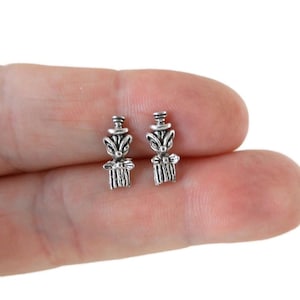 May include: A pair of silver stud earrings featuring a whimsical design of a small animal wearing a hat. The animal appears to be a fox or a squirrel.