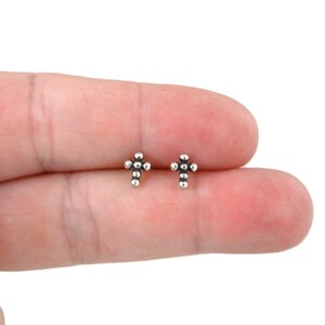 May include: A pair of silver cross stud earrings. Each earring is made of small silver beads in the shape of a cross.
