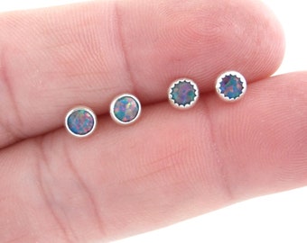 Puede incluir: Cuatro pendientes de plata con piedras de ópalo iridiscente. Los pendientes están dispuestos en una fila en un dedo.
