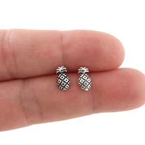 May include: A pair of silver pineapple stud earrings. The earrings are small and delicate, and they feature a detailed pineapple design.