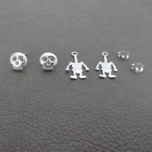 May include: A set of silver earring findings featuring a skull and skeleton design. The set includes two skull earrings, two skeleton charms, and two earring backs.