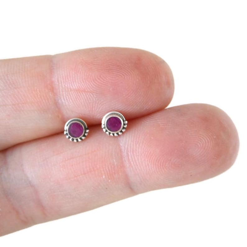 May include: A pair of silver stud earrings with small round pink gemstones set in a beaded border.