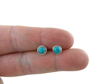 May include: A pair of silver stud earrings with turquoise stones. The earrings are small and round, and the stones are a bright blue colour.