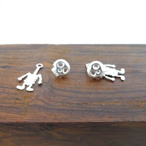 May include: A pair of silver skull earrings with a dangling skeleton charm. The earrings are on a wooden surface.