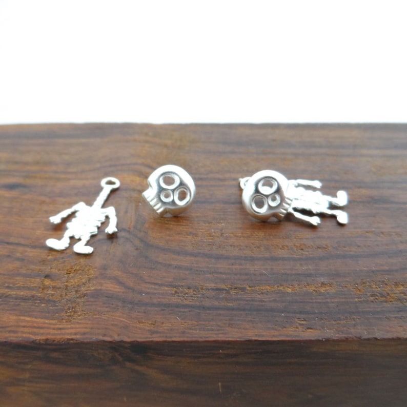 May include: A pair of silver skull earrings with a dangling skeleton charm. The earrings are on a wooden surface.