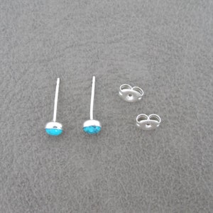 May include: A pair of silver stud earrings with turquoise stones. The earrings have a post and butterfly back.