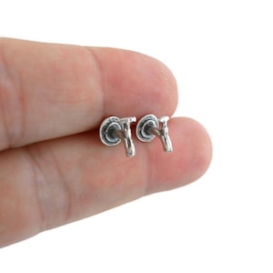 May include: A pair of silver faucet stud earrings. The earrings are small and delicate, and they feature a realistic design of a faucet.