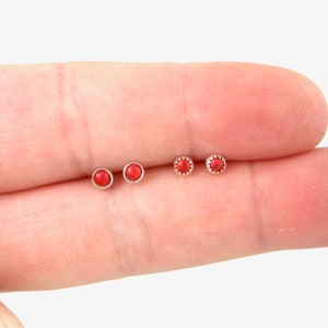 May include: Four small red gemstone earrings with silver settings. The earrings are displayed on a finger.