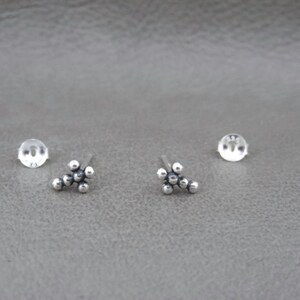 May include: A pair of silver stud earrings with a cluster of small round beads in the shape of a cross.