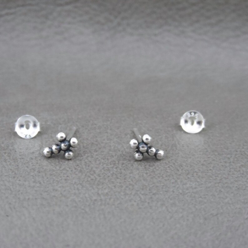May include: A pair of silver stud earrings with a cluster of small round beads in the shape of a cross.
