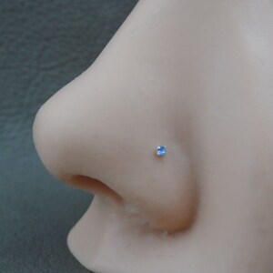May include: A close-up of a nose piercing with a small, light blue gemstone.