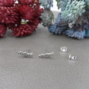 Puede incluir: Un par de pendientes de plata con forma de trompeta. Los pendientes son pequeños y delicados, y presentan un diseño detallado de una trompeta.