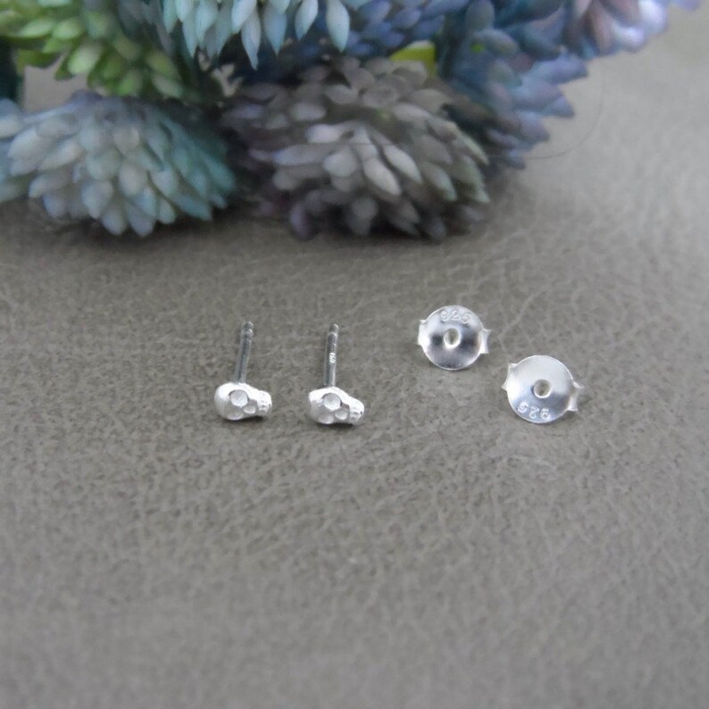 May include: A pair of silver skull stud earrings with a 925 stamp on the back.