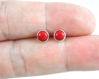 May include: A pair of small, round, red gemstone earrings with silver settings.