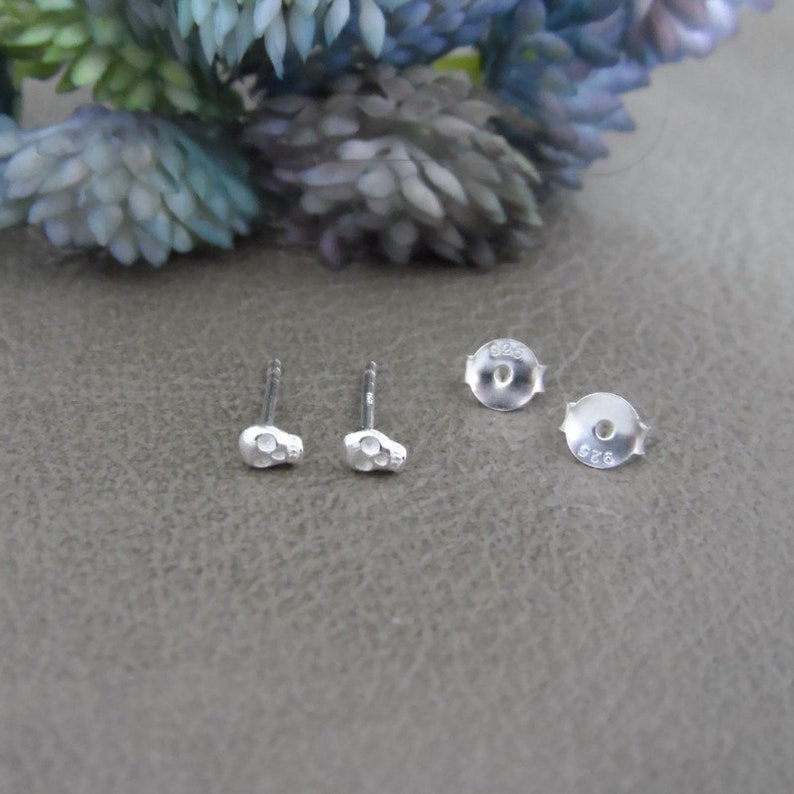 May include: A pair of silver skull stud earrings. The earrings are small and have a detailed skull design. The backs of the earrings are marked with the number 925.