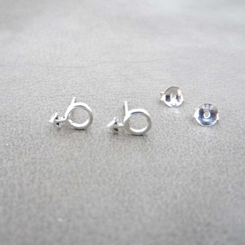 May include: A pair of silver earrings with a male symbol design. The earrings are marked with "925", indicating they are made of sterling silver.