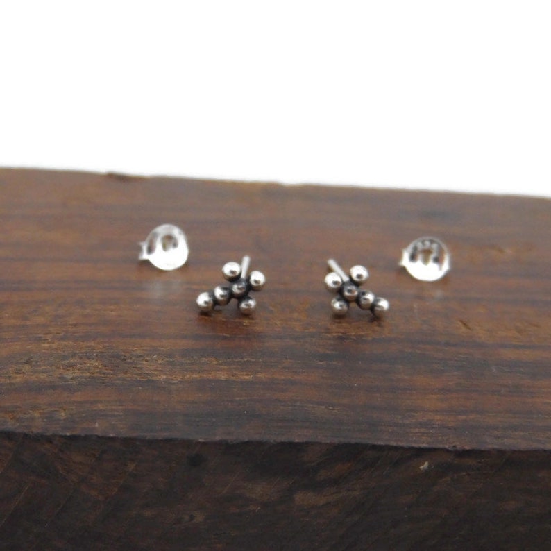May include: A pair of silver stud earrings with a cluster of small, round beads in the shape of a flower.