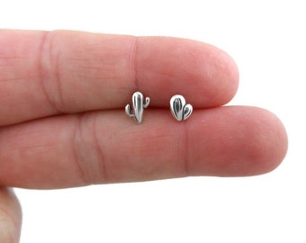 May include: A pair of silver cactus stud earrings. One earring features a single cactus with a small arm, while the other earring features two small cacti.