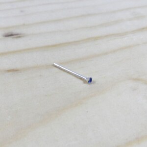 Op de afbeelding: Een zilveren neuspiercing met een kleine blauwe edelsteen.
