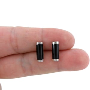 May include: A pair of black onyx stud earrings with silver trim. The earrings are cylindrical in shape and are shown on a finger.