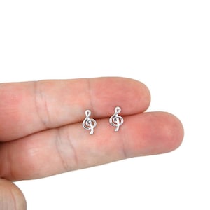 Puede incluir: Un par de pendientes de plata con forma de clave de sol. Los pendientes son pequeños y delicados, y son perfectos para añadir un toque de música a cualquier atuendo.