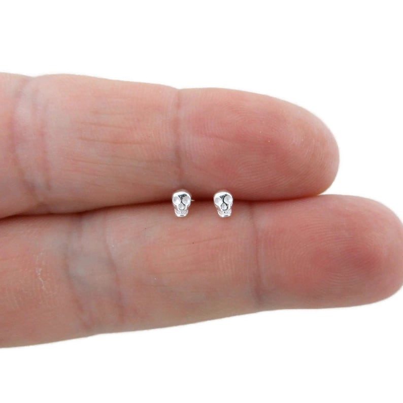 May include: A pair of silver skull stud earrings. The earrings are small and delicate, and they are perfect for adding a touch of edgy style to any outfit.
