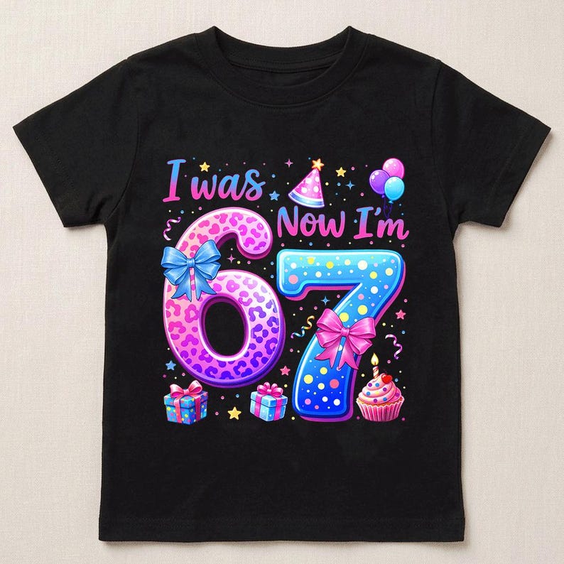 May include: A black short-sleeve t-shirt featuring a colorful graphic with the text I was 6, Now I'm 7. The design includes a pink leopard print number 6 with a blue bow, a blue polka dot number 7 with a pink bow, party hats, balloons, and a cupcake.