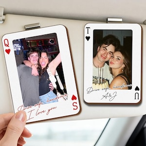 Può includere: Due clip per visiera parasole per auto a forma di carte da gioco con foto. Uno mostra una coppia con il testo "Drive safe, handsome. I love you." L'altro mostra una coppia con il testo "Drive safe, handsome. A&J."