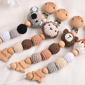 Op de afbeelding: Baby fopspeenclips met houten kralen en gehaakte dierenkoppen. Elke clip heeft een stervormig houten stuk met een gegraveerde naam. De dierenkoppen zijn onder andere een koala, aap, beer en vos. De clips zijn in verschillende kleuren.