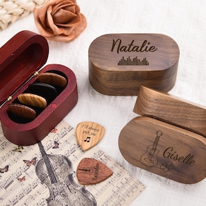 May include: Wooden guitar pick boxes and picks. One box is open, revealing picks. Two boxes are closed, one with the name "Natalie" and a sound wave design, the other with "Giselle" and a guitar illustration. Two picks have text.