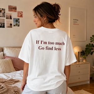 Może przedstawiać: Biały t-shirt z krótkim rękawem z ciemnoczerwonym napisem "If I'm too much Go find less" nadrukowanym na plecach. Koszulka ma okrągły dekolt i luźny, swobodny krój, widoczna od tyłu na sylwetce osoby.