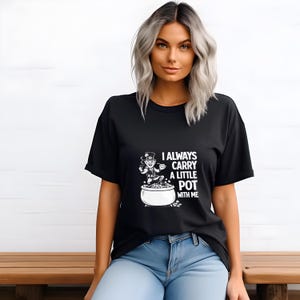 May include: Black t-shirt with the text "I always carry a little pot with me." The graphic shows a leprechaun with a pot of gold. The shirt is worn by a person with light hair and blue jeans.