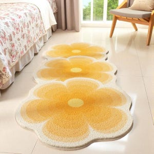 May include: Three daisy-shaped rugs in yellow and cream hues. The rugs are arranged in a line, featuring a textured surface. The design is reminiscent of a daisy or sunflower. Each rug is approximately 100 cm in diameter.