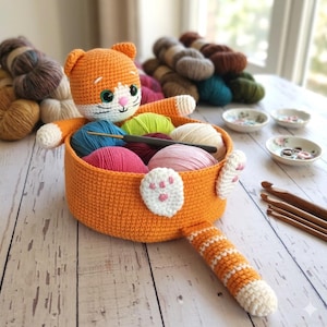 May include: An orange crochet cat basket filled with colorful yarn balls. The cat has white paws, a white face, and a striped tail. Crochet hooks and small decorative dishes are also visible on the wooden surface.