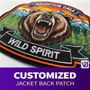 Może przedstawiać: Haftowana naszywka na plecy kurtki z ryczącym niedźwiedziem i napisem "WILD SPIRIT" na czarnym banerze. Naszywka zawiera również napis "MOUNTAIN CALL" oraz scenę gór i lasu. Na dole naszywki widnieje napis "CUSTOMIZED JACKET BACK PATCH".