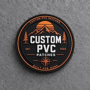 May include: A circular black PVC patch featuring an orange mountain and sunset graphic, two pine trees, and a compass rose. The text reads CUSTOM PVC PATCHES, EST. 2024, and BUILT FOR MORE in white and orange lettering against the black background.