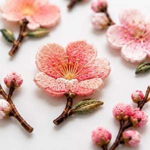 Könnte beinhalten: Mehrere gestickte Kirschblüten-Aufnäher mit rosa und weißen Blütenblättern und gelben Zentren, befestigt an braunen Stielen mit grünen Blättern und kleinen rosa Knospen. Die detaillierte Stickerei erzeugt ein strukturiertes Blumenmuster.
