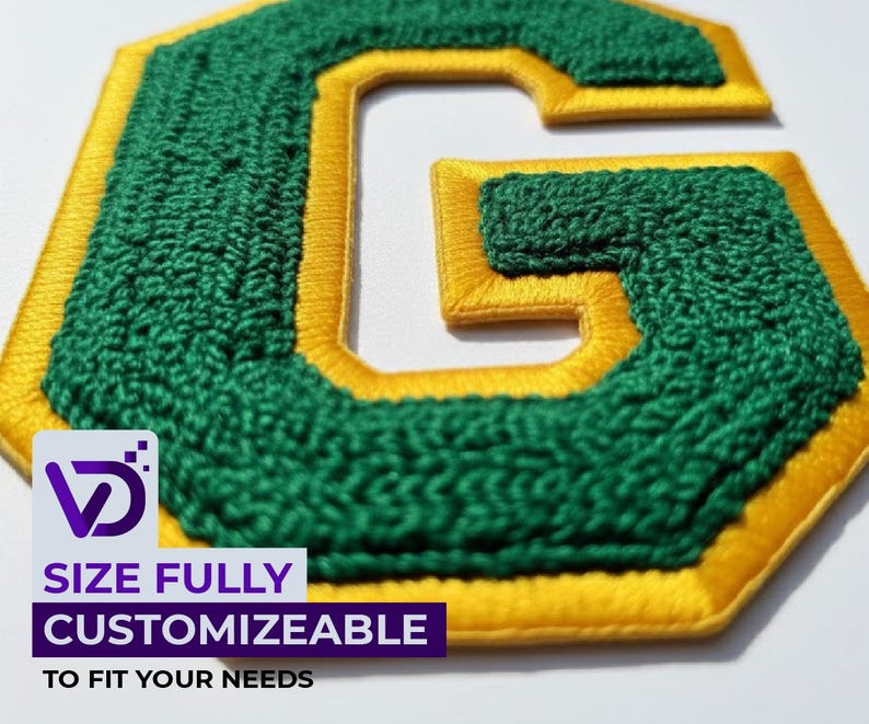 以下が含まれることがあります： 緑と金の刺繍入り文字「G」のパッチのクローズアップ。文字は質感のある緑色の生地で埋められ、金色の糸で縁取られています。パッチは白い背景にあります。下部のテキストは「SIZE FULLY CUSTOMIZEABLE TO FIT YOUR NEEDS」と書かれています。