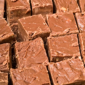 May include: Close-up of several squares of chocolate fudge. The fudge is a medium brown color with a slightly textured surface. The squares are cut evenly and arranged closely together, showcasing a homemade treat.
