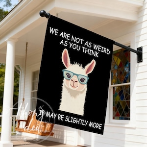 Könnte beinhalten: Schwarze Outdoor-Flagge mit einem weißen Lama, das eine blaue Brille trägt. Die Flagge trägt den weißen Text "WE ARE NOT AS WEIRD AS YOU THINK, IT MAY BE SLIGHTLY MORE". Die Flagge hängt an einer schwarzen Stange.