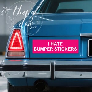 May include: A blue car's rear with a bright pink bumper sticker that reads "I HATE BUMPER STICKERS." The car has a red triangular tail light and a chrome bumper.