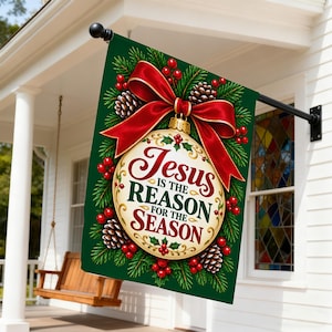 Könnte beinhalten: Eine rechteckige Gartenflagge mit dunkelgrünem Hintergrund und einer cremefarbenen Weihnachtskugel in der Mitte. Das Ornament zeigt den Text 'Jesus IS THE REASON FOR THE SEASON' in Rot und Grün, umgeben von Tannenzweigen, Tannenzapfen, roten Beeren und einer großen roten Schleife.
