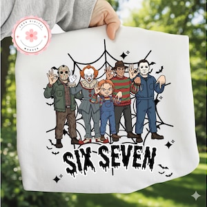 May include: White tote bag featuring a graphic of six horror movie characters, including Jason, Pennywise, Chucky, Freddy Krueger, and Michael Myers, arranged in front of a spiderweb design. The text "SIX SEVEN" is printed in black below the characters.