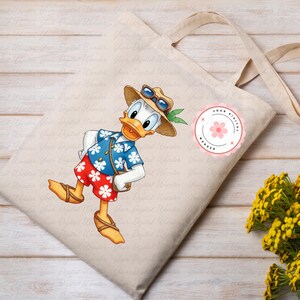 May include: Beige canvas tote bag featuring a cartoon image of Donald Duck in a Hawaiian shirt, sunglasses, and a straw hat. The bag has long handles and a round pink sticker with text. Yellow flowers are in the background.