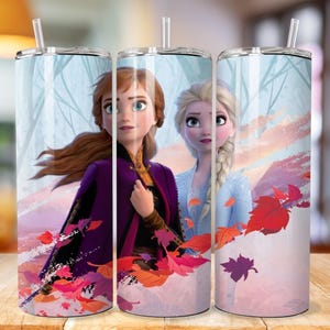 May include: Two stainless steel tumblers featuring a design of the characters Anna and Elsa from the film Frozen. The design includes a wintry background with falling leaves in shades of red, orange, and purple.