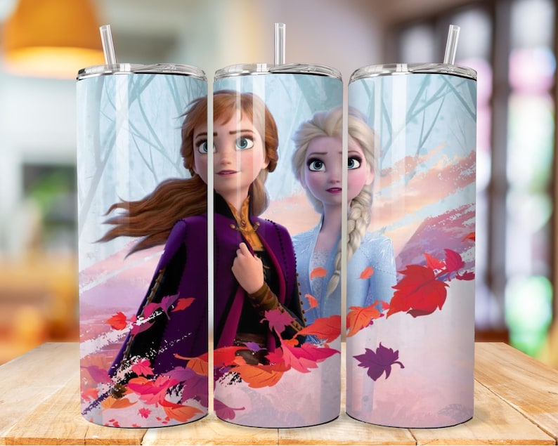 May include: Two stainless steel tumblers featuring a design of the characters Anna and Elsa from the film Frozen. The design includes a wintry background with falling leaves in shades of red, orange, and purple.